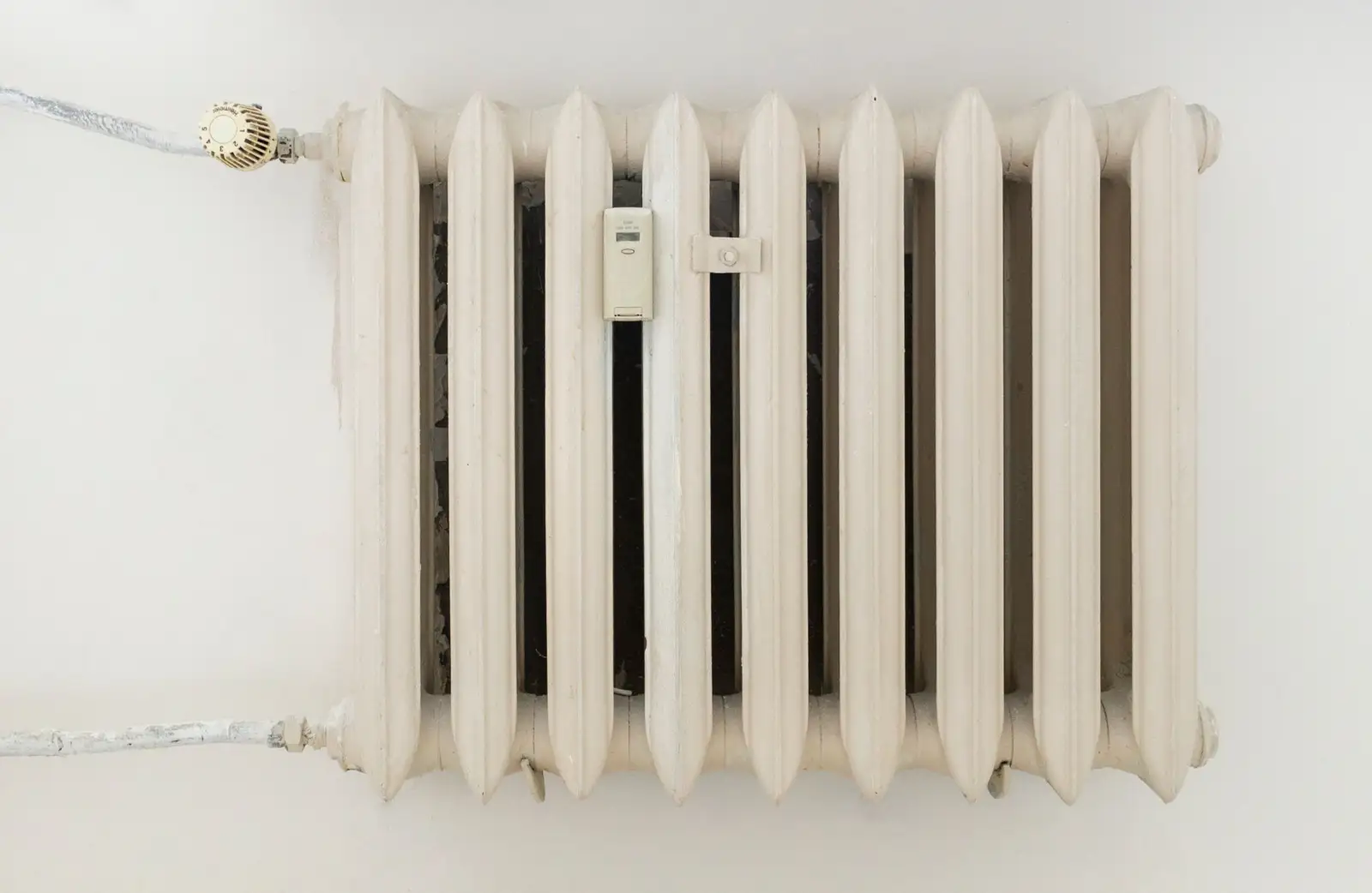 Radiateur en fonte à colonnes peint en blanc, avec une tête thermostatique graduée de 1 à 5 sur son robinet d'entrée et un répartiteur de frais de chauffage fixé au centre