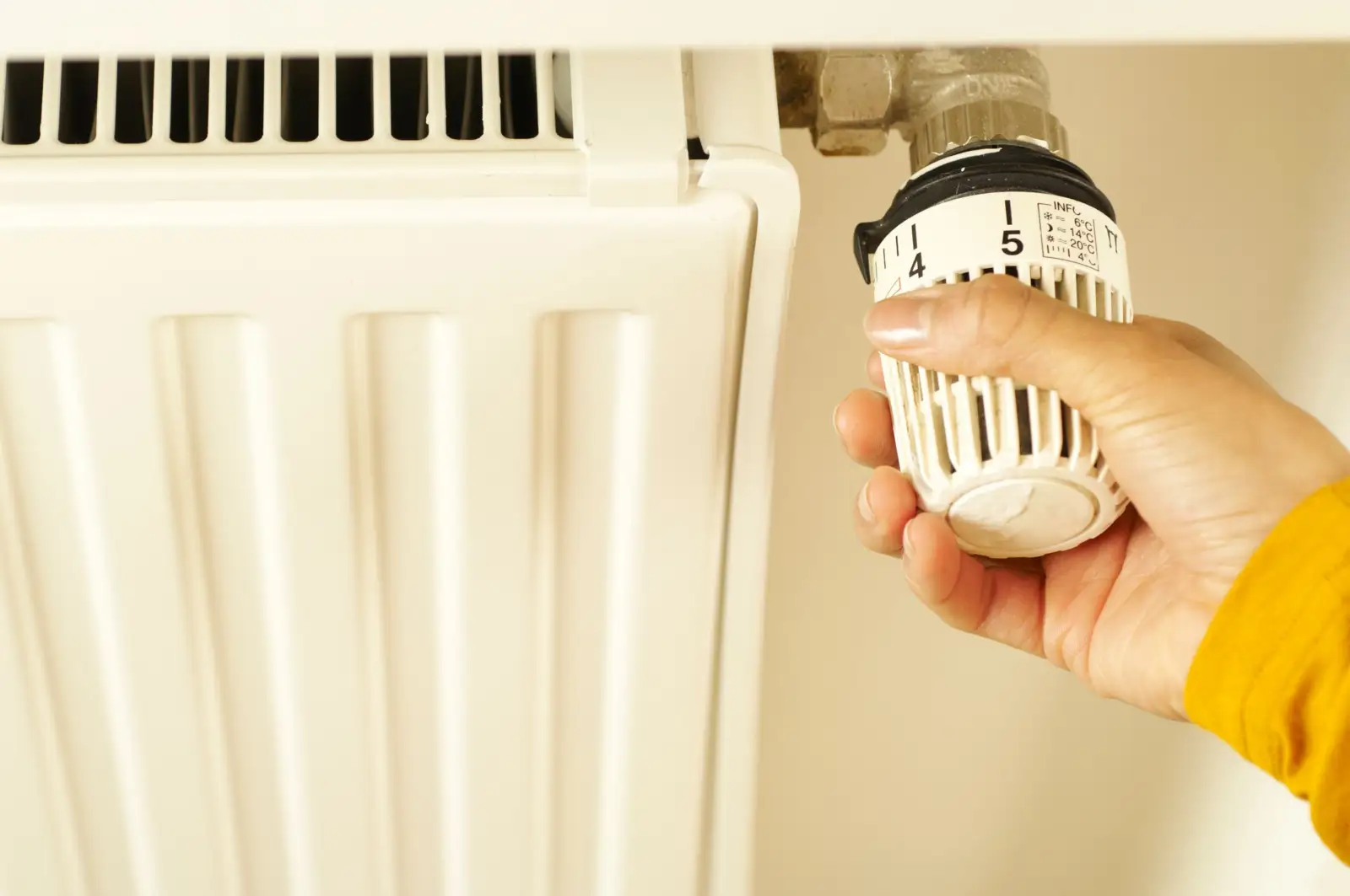 Main qui tourne la tête thermostatique blanche graduée d'un radiateur à panneaux
