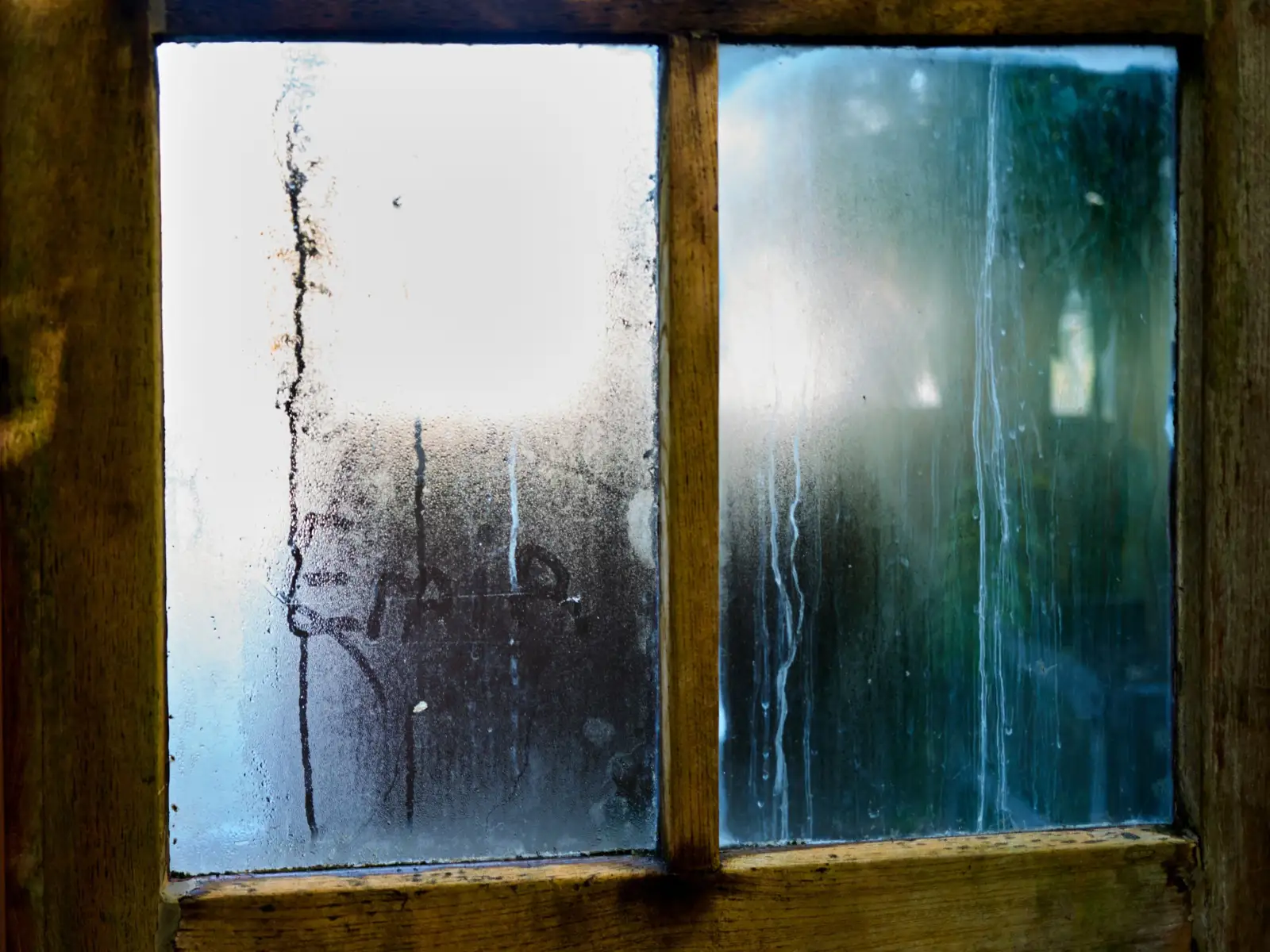 Buée et coulures de condensation sur les carreaux d'une fenêtre à croisillons en bois