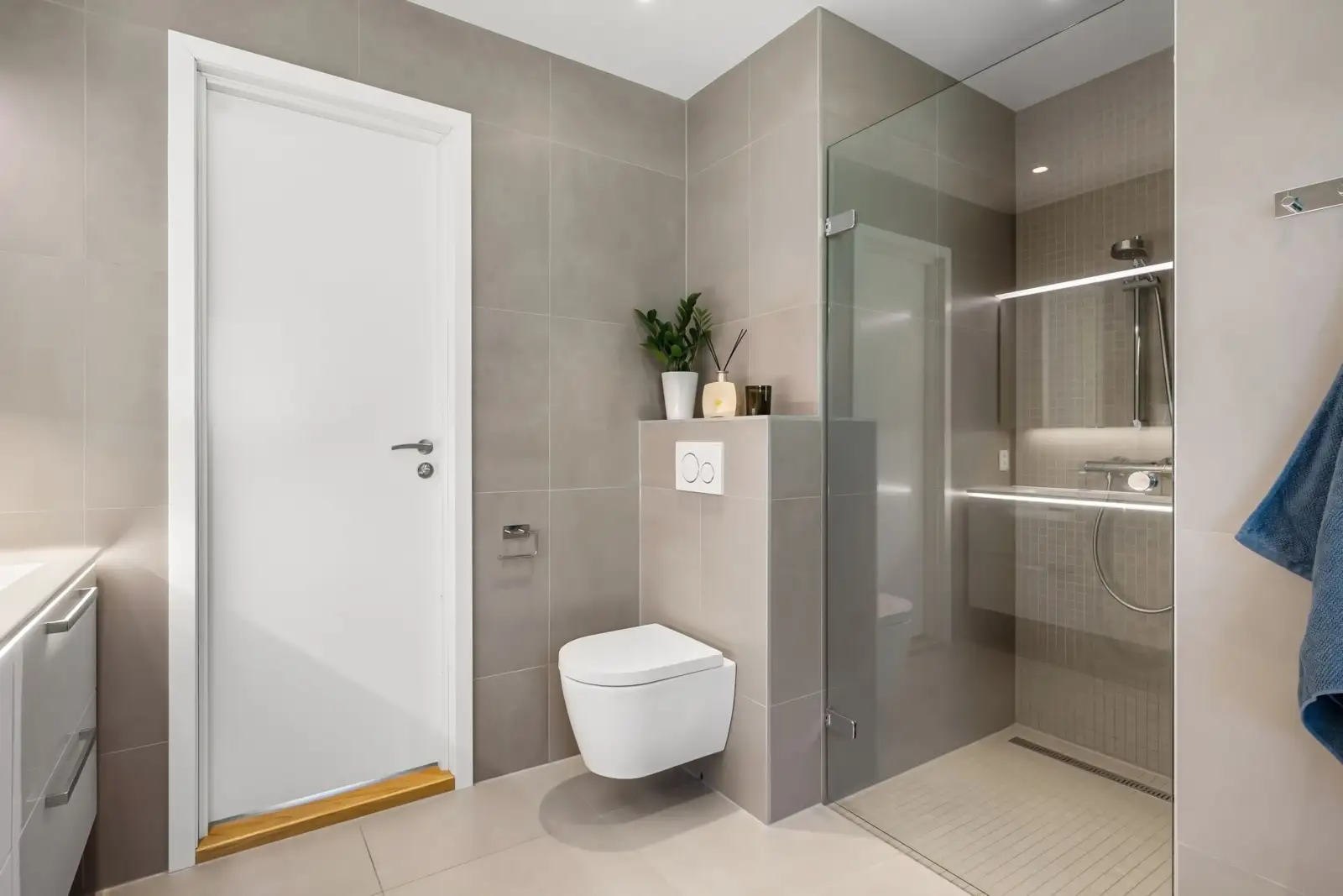WC suspendu blanc devant un coffrage carrelé à mi-hauteur portant la plaque de commande, à côté d'une douche à l'italienne vitrée