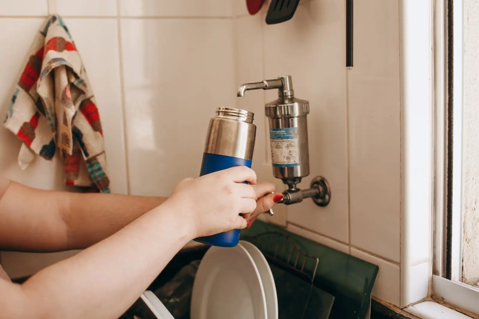 Main remplissant une gourde isotherme à un robinet de cuisine équipé d'un filtre en inox