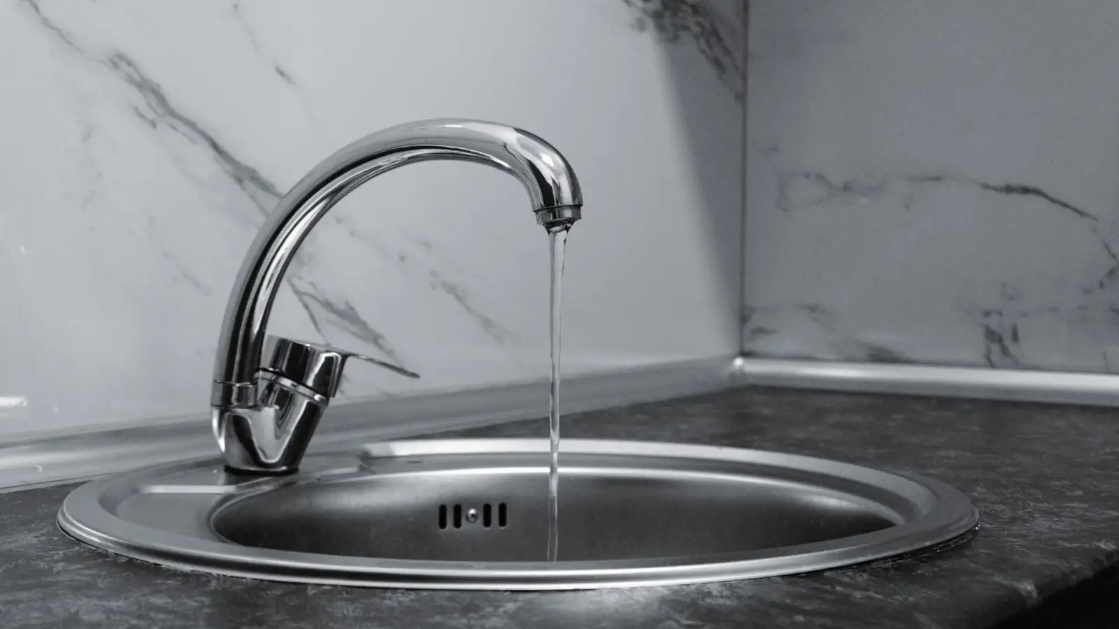 Robinet de cuisine chromé dont l'eau coule dans un évier rond en inox