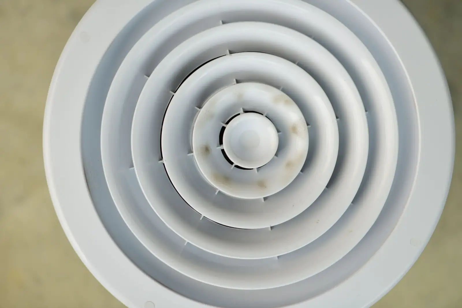 Grille de ventilation ronde en plastique blanc vue de face, avec des traces de poussière sur ses anneaux centraux