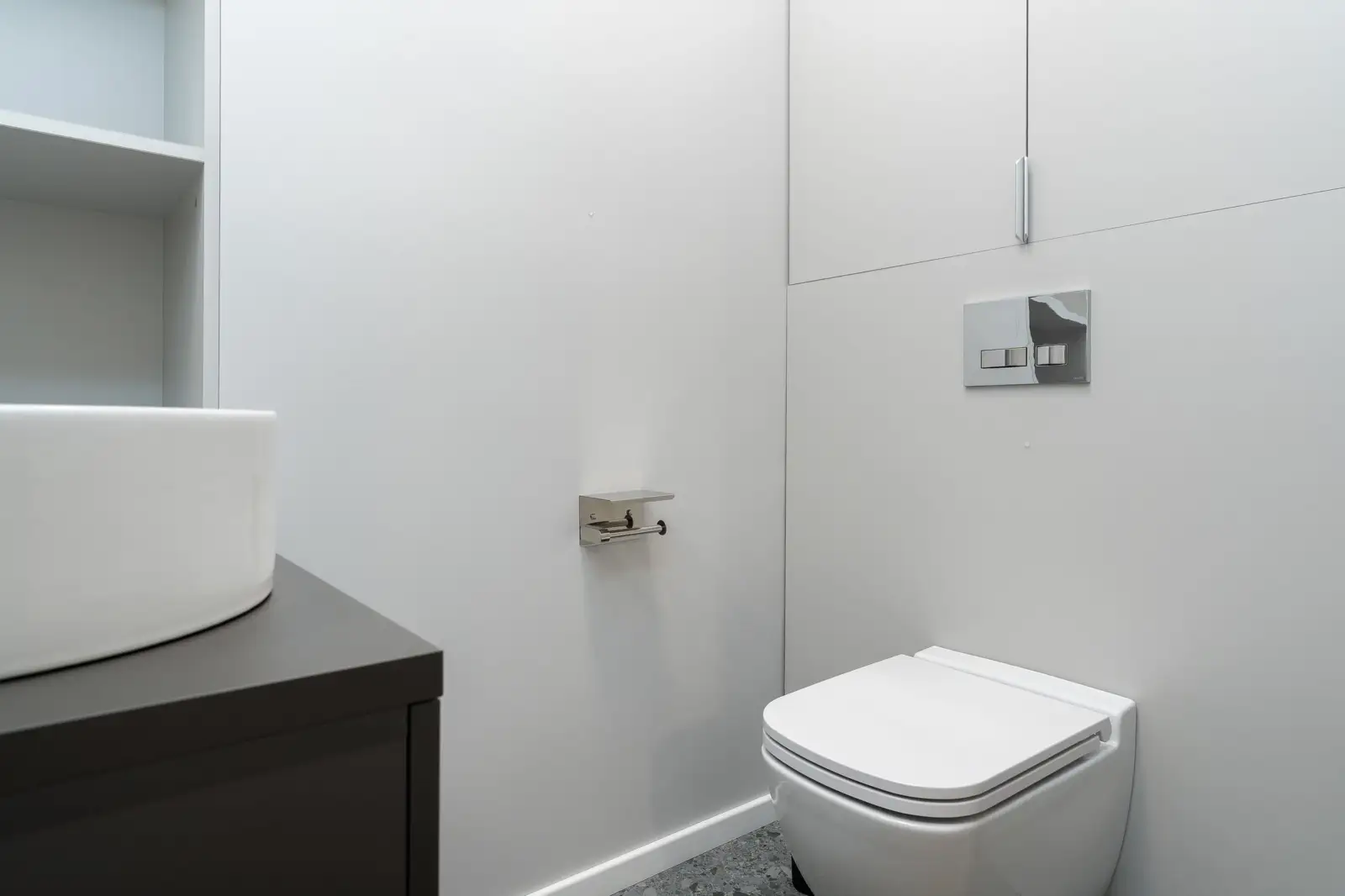 WC suspendu blanc sous une plaque de commande chromée à double touche fixée au mur