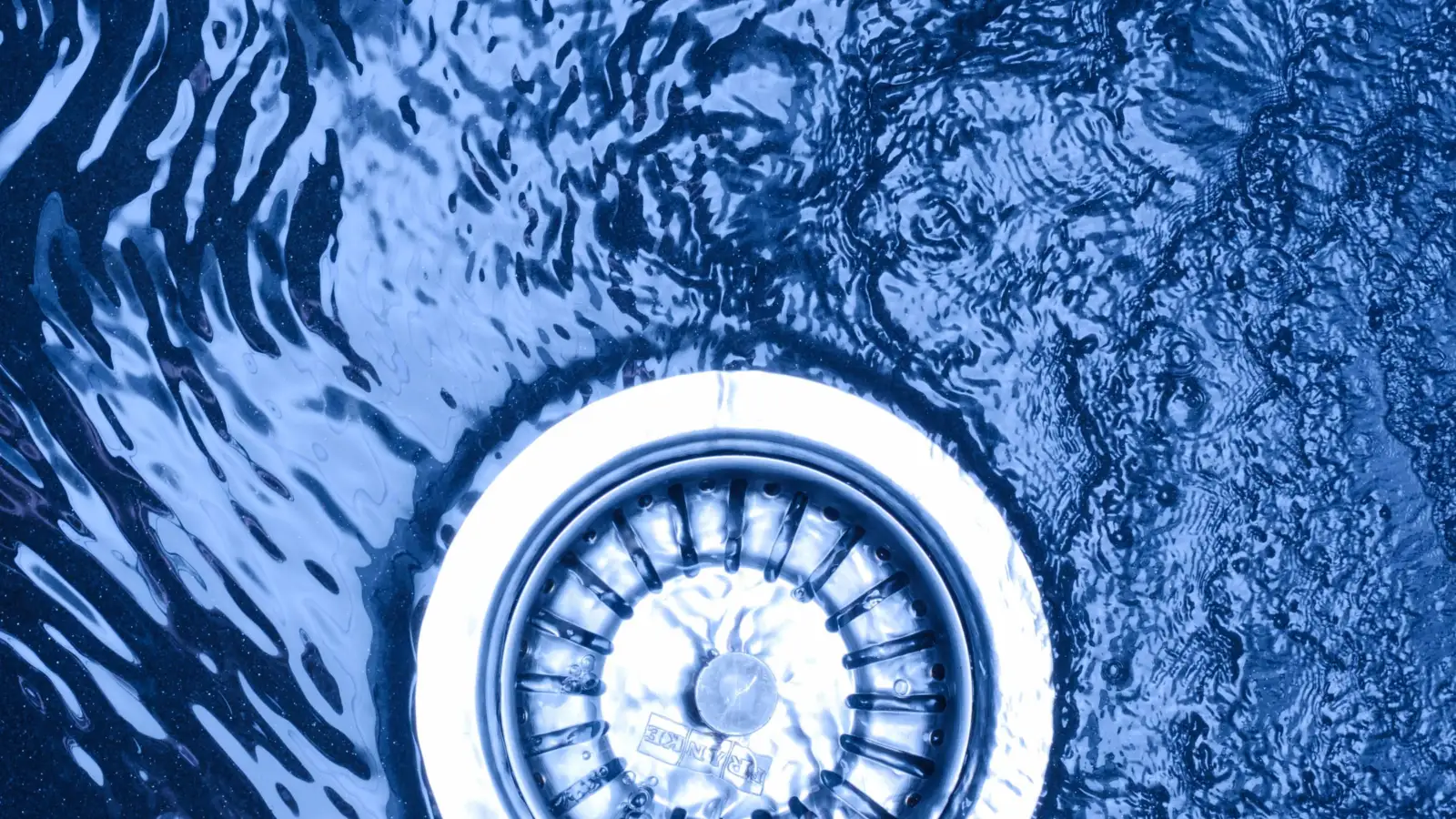 Eau qui tourbillonne vers la bonde à panier d'un évier en inox, sous une lumière bleutée