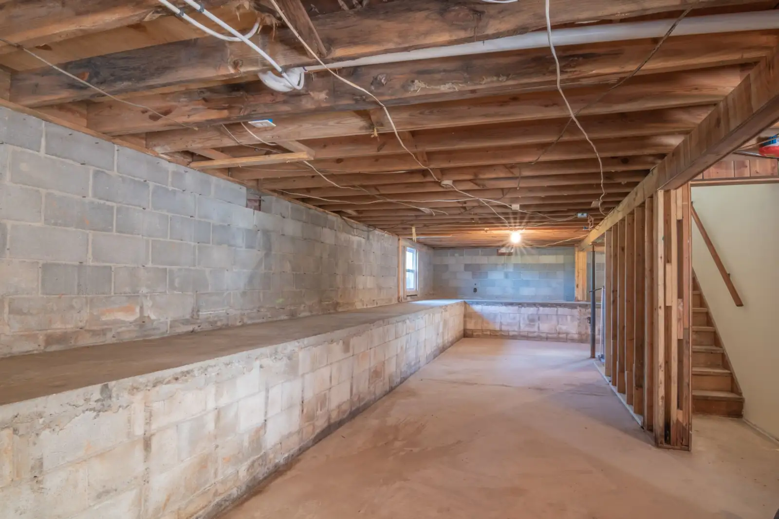 Sous-sol vide aux murs en blocs de béton, poutres de plancher apparentes et escalier en bois
