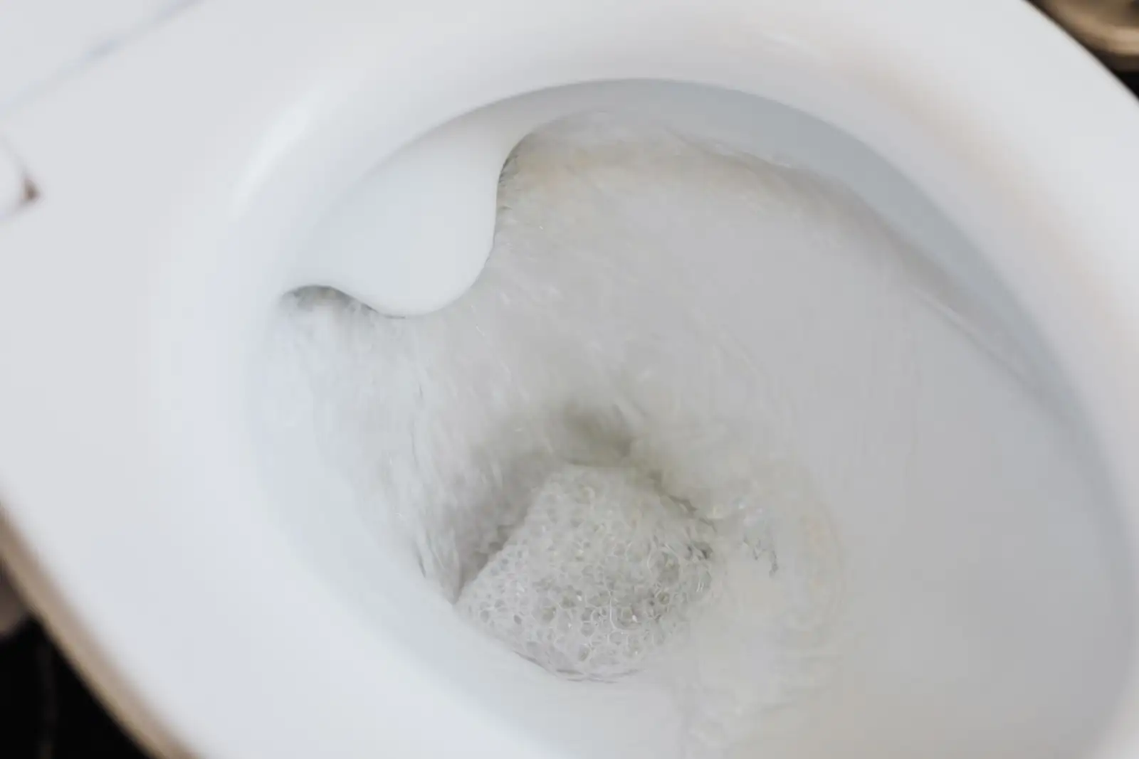 Eau de chasse qui tourbillonne au fond d'une cuvette de WC en céramique blanche
