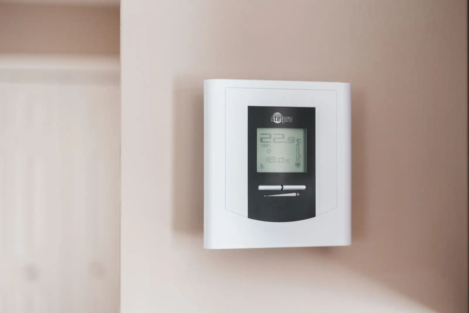 Thermostat d'ambiance numérique blanc fixé sur une cloison intérieure, écran affichant 22,5 °C et 18,0 °C