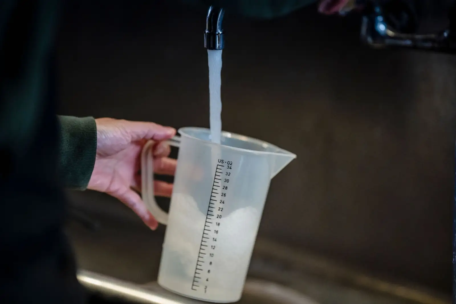 Main tenant un pichet doseur gradué en plastique qui se remplit sous un robinet
