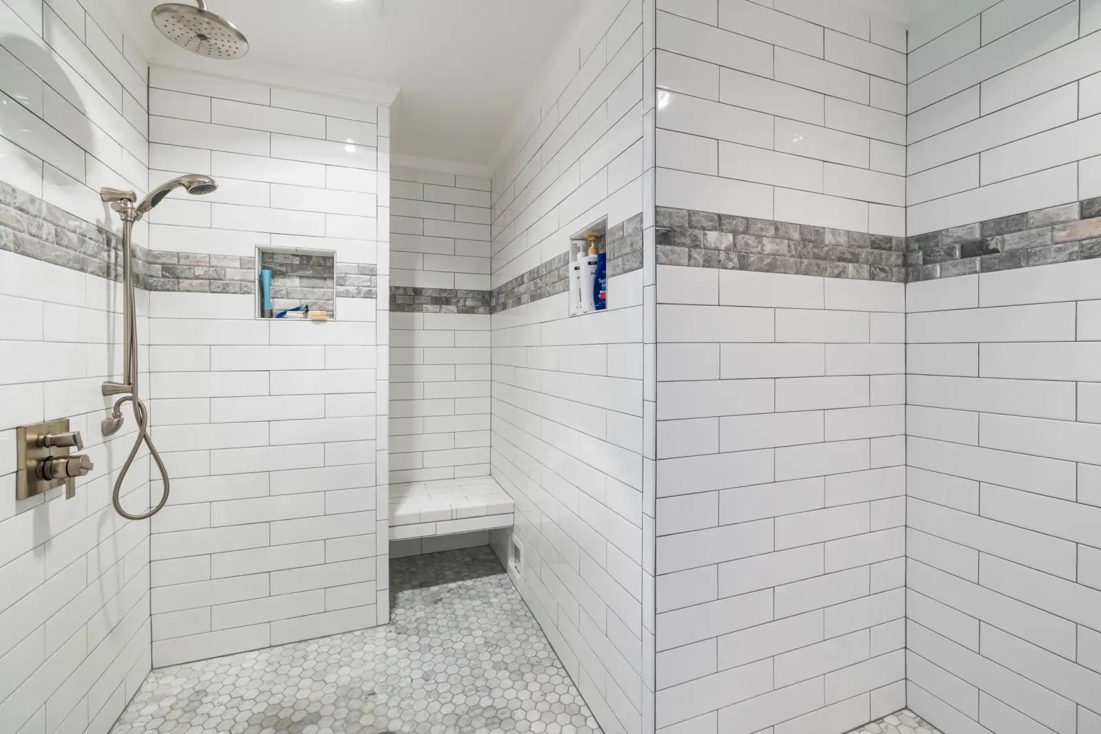 Douche de plain-pied carrelée en blanc avec sol en mosaïque hexagonale, tête de douche au plafond, douchette sur barre et commandes encastrées