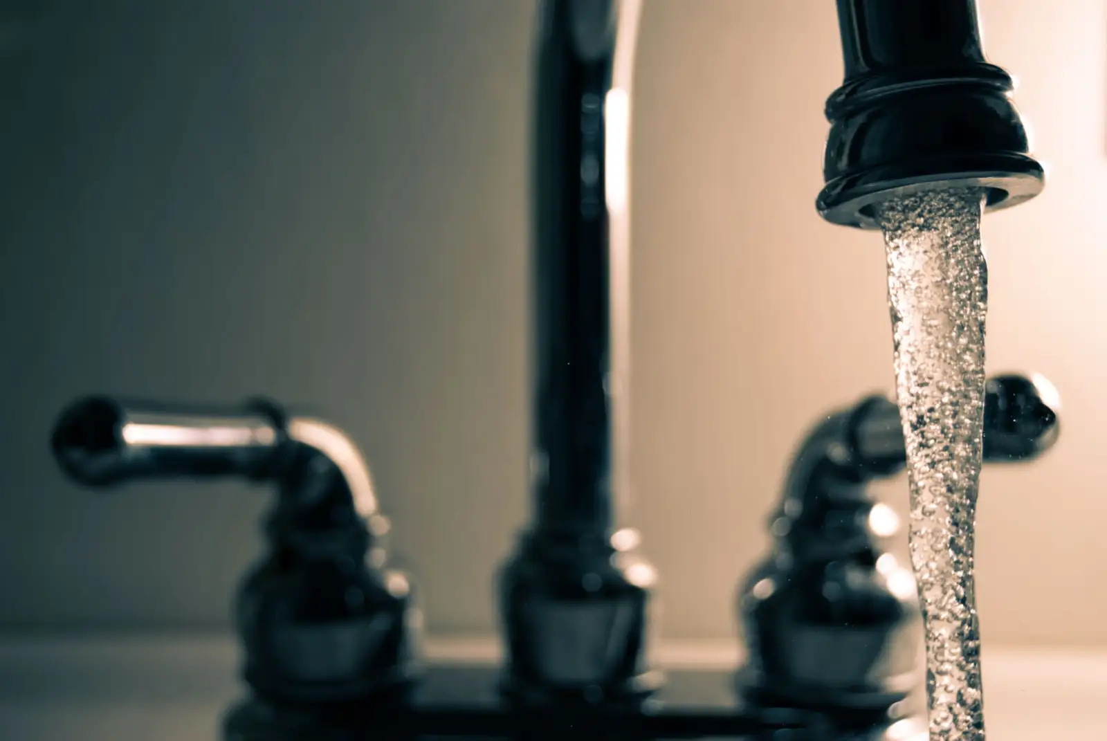 Filet d'eau qui s'écoule d'un bec de robinet métallique, devant les deux manettes du mélangeur, en gros plan